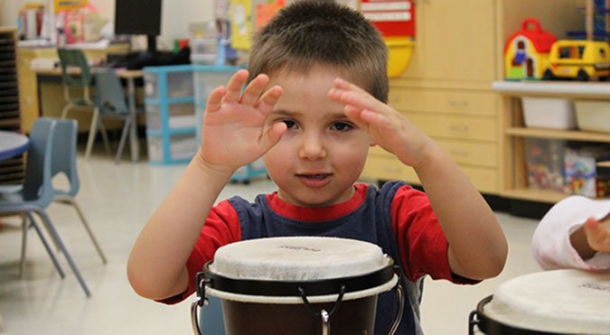 A child drums on a wooden drum with his hands at a PLASP program