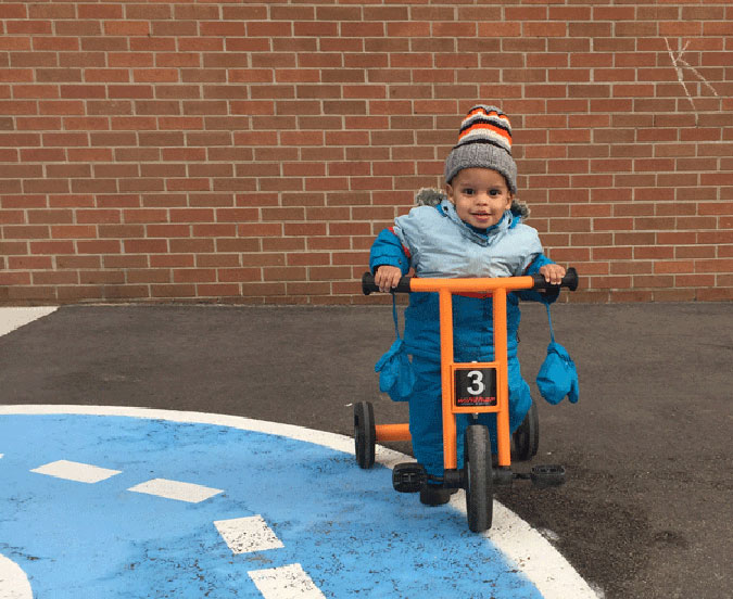 A child in winter clothing rides a tricycle outdoors 