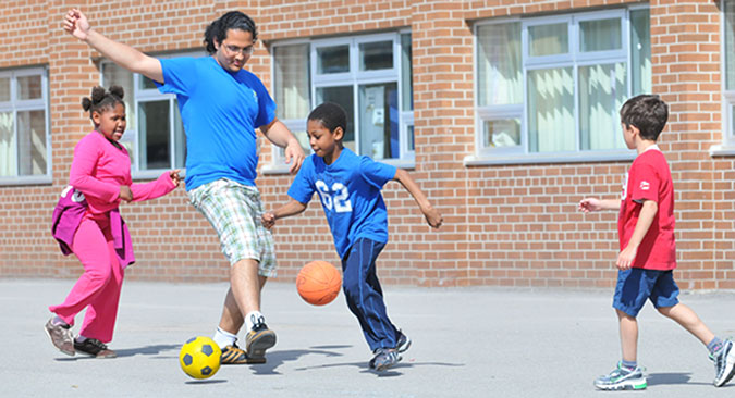 A PLASP staff member plays soccer with two children 