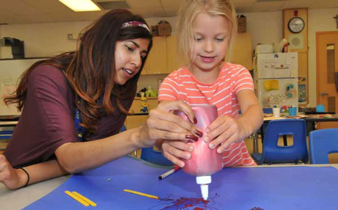 A PLASP staff member paints with a child using a squirt bottle 