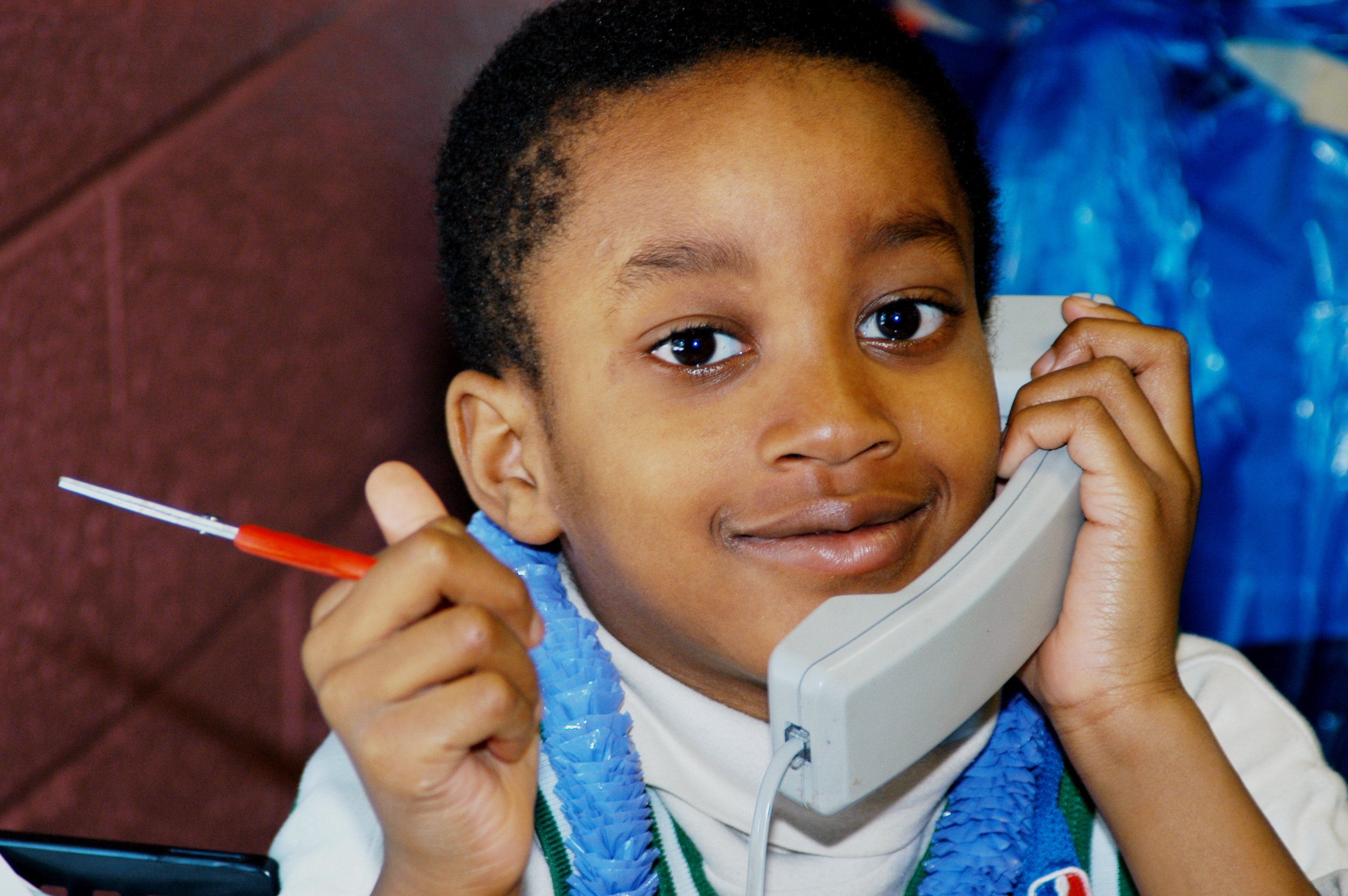 A boy in a PLASP wearing a blue plastic necklace answers a phone