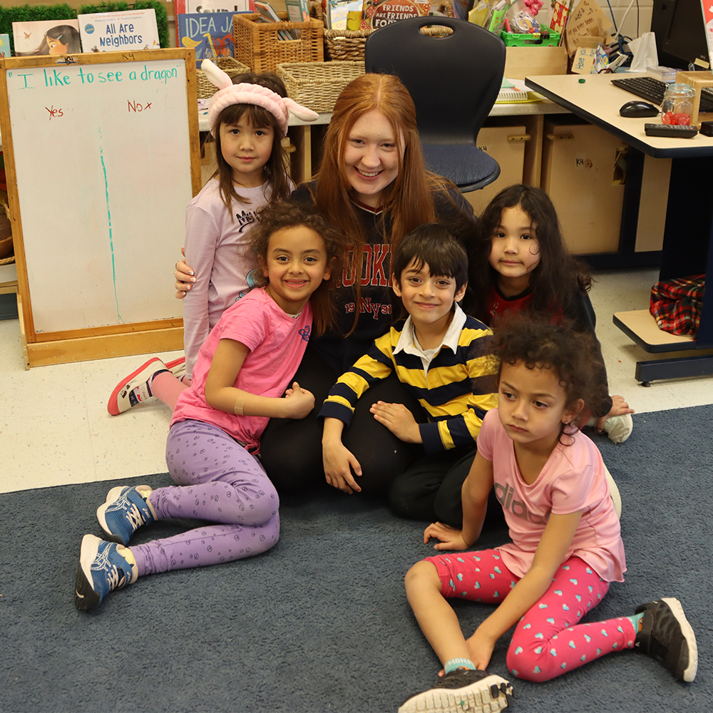 A volunteer sits with kids in a PLASP program classroom 