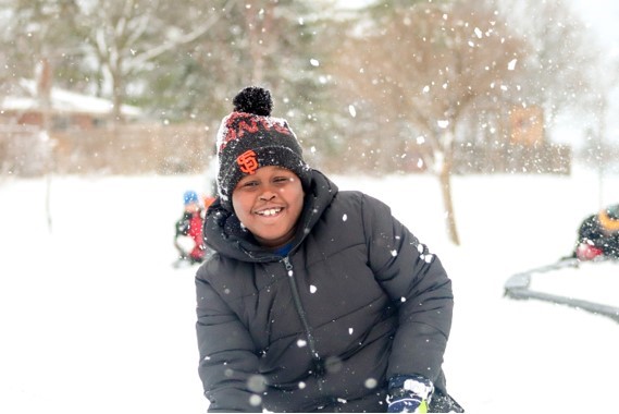 A boy in a PLASP program wearing warm winter clothes and a hat smiles during outdoor time