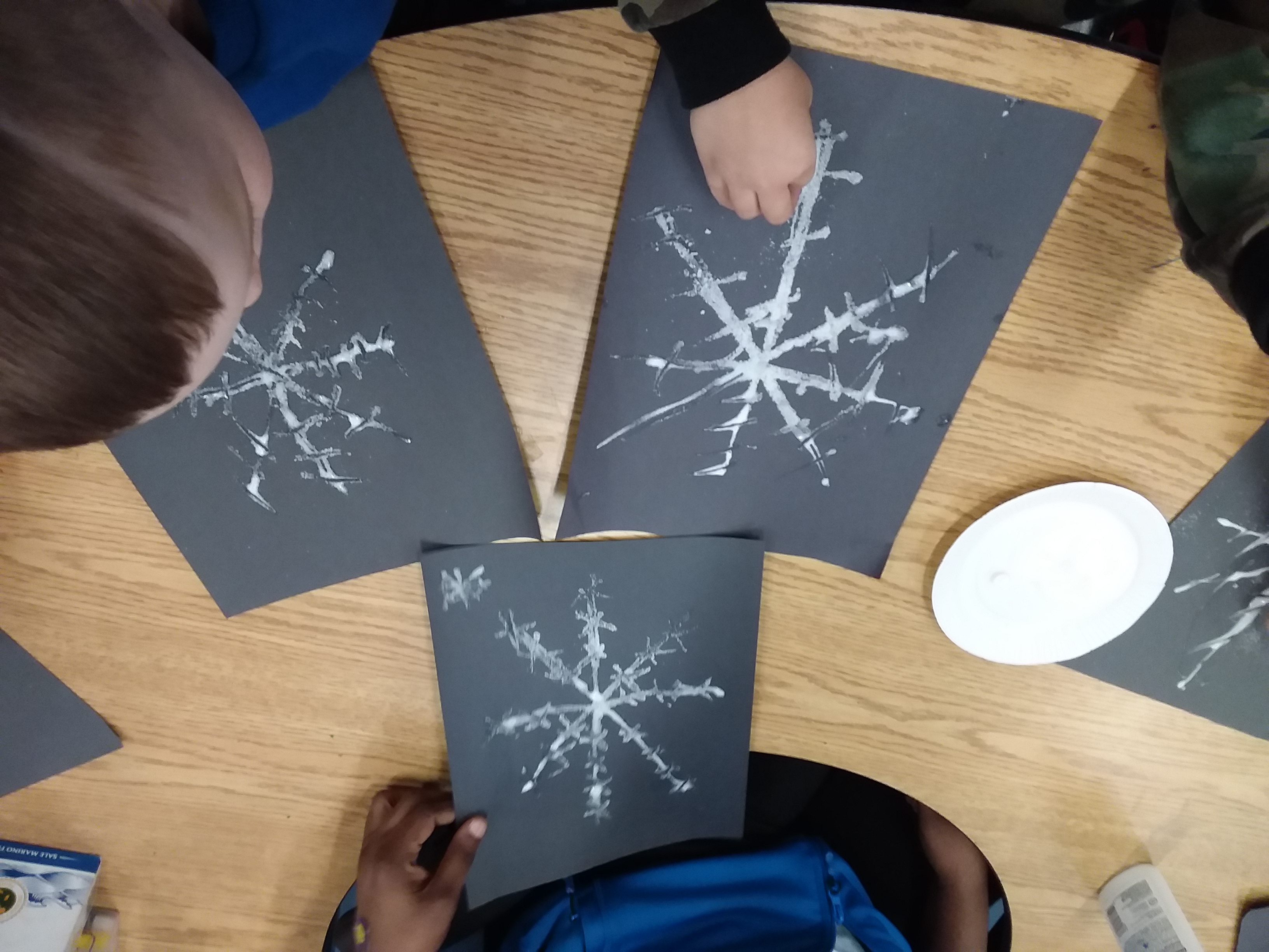 Friends drawing snowflakes on black paper with white paper