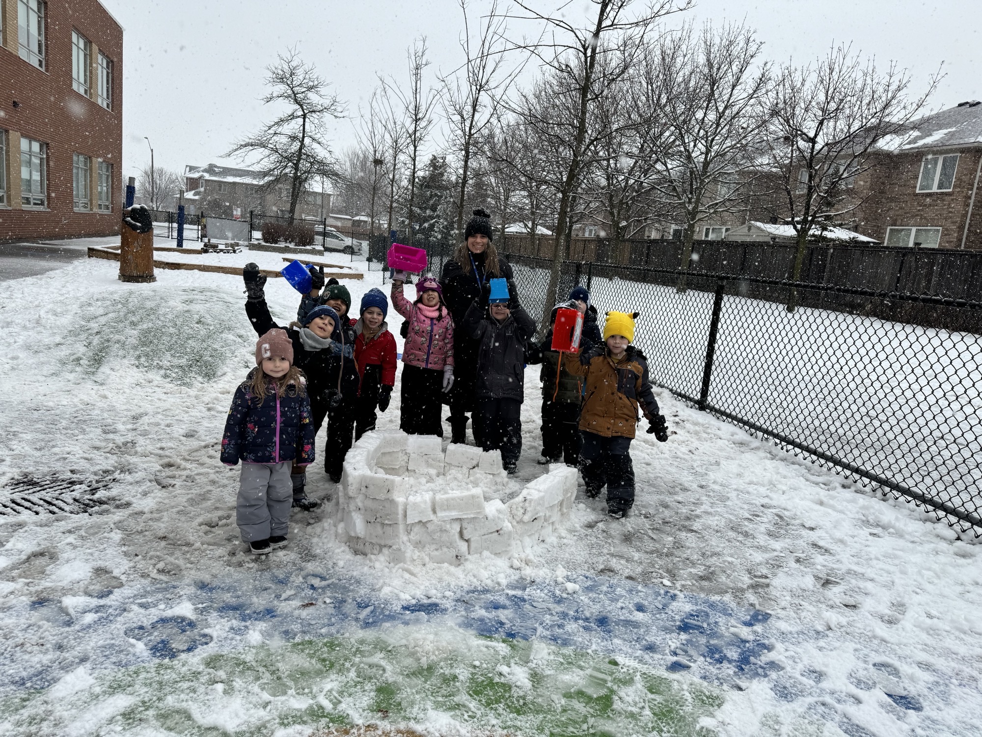 A group of friends stand around their snow structure, waving 