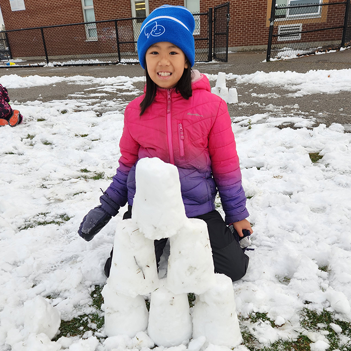 A girl in a PLASP program kneels in front of a snow pyramid